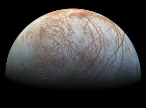 Half the sphere of Europa, an icy white moon with red streaks over its surface